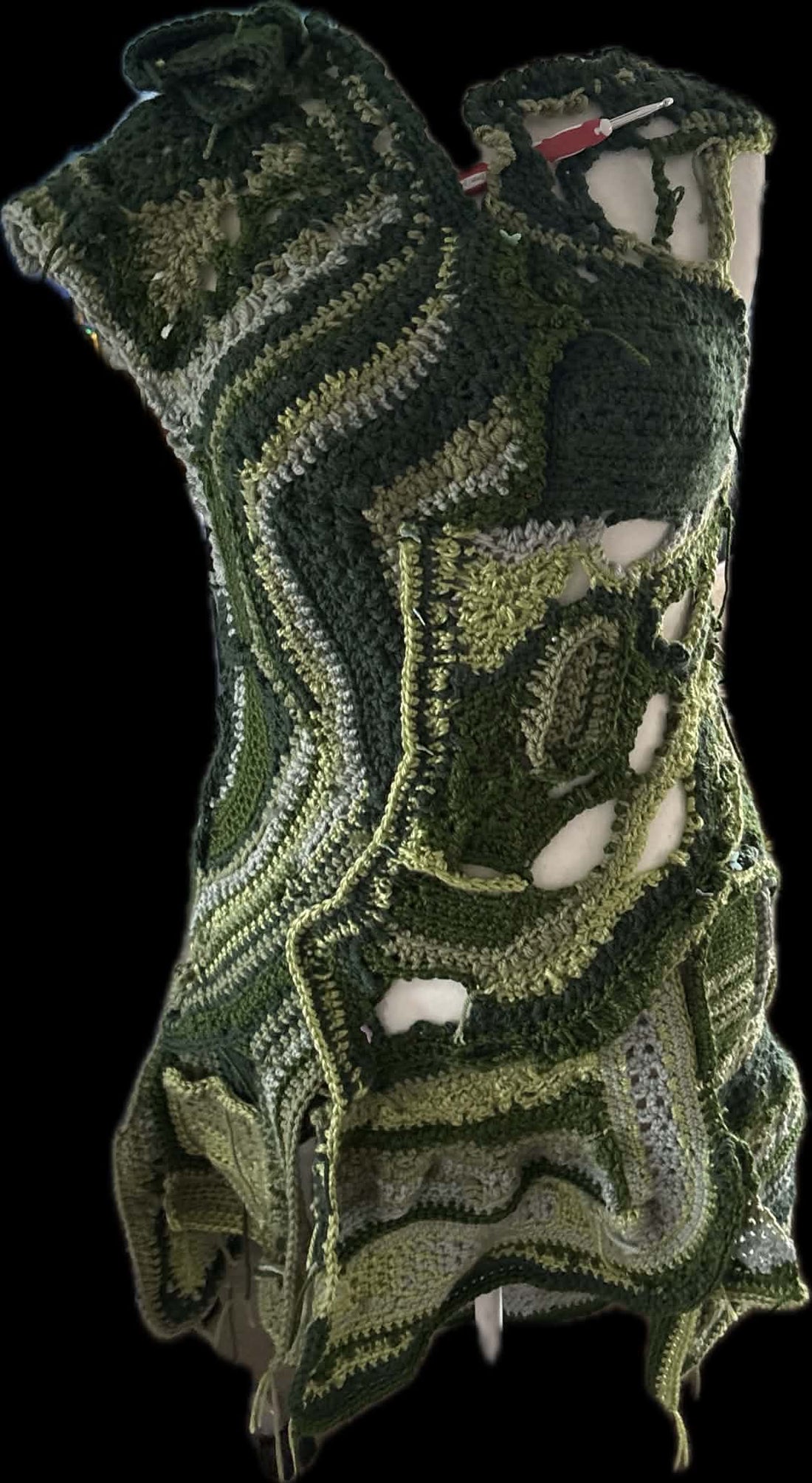 An in-progress shot of the handmade crocheted Boudica coat on a mannequin, showcasing organic freeform stitchwork in shades of forest green, olive, and sage, designed to later feature custom leather patches.