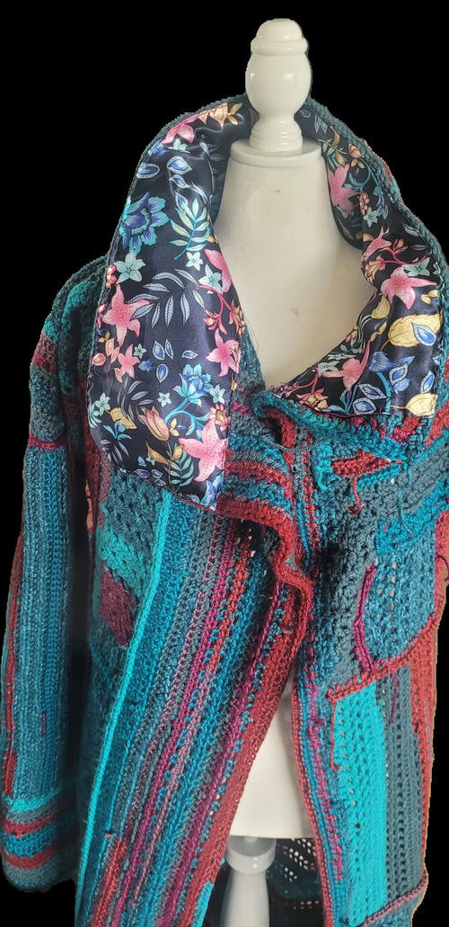 A multicolor crochet knit cardigan with a large floral-patterned collar, displayed on a white mannequin torso against a black background.